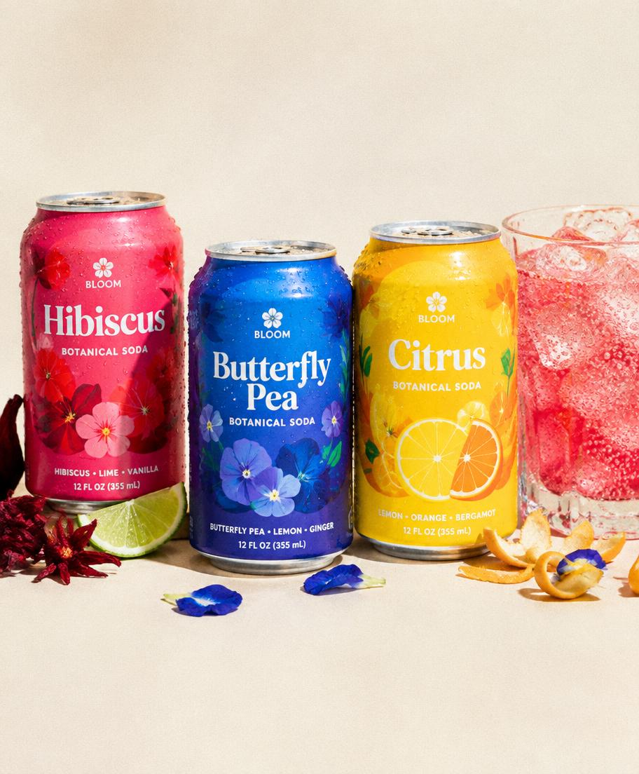Three colorful botanical soda cans beside a glass of fizzy drink
